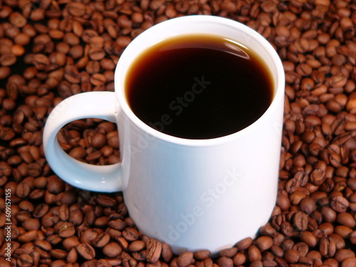 A hot cup of coffee surrounded by whole coffee beans