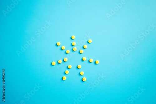 A sun of yellow pills from a bottle on a blue background.