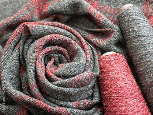 Woven red and gray tweed scarf or shawl and bobbins with threads. Everyday warm clothes