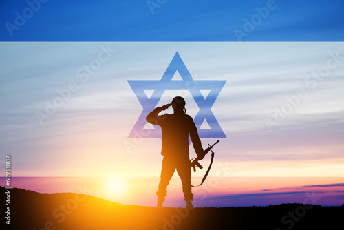 Silhouette of soldier saluting against the sunrise in the desert and Israel flag.