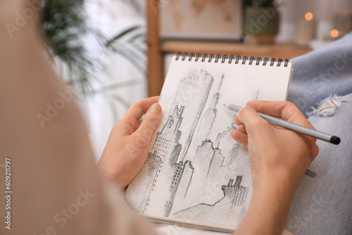 Woman sketching cityscape in notebook with pencil at home, closeup