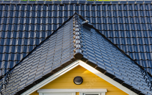 Black glossy ceramic roof shingles on a yellow house.