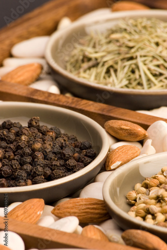 Black peppercorns and various Spices close up in a wooden tray.