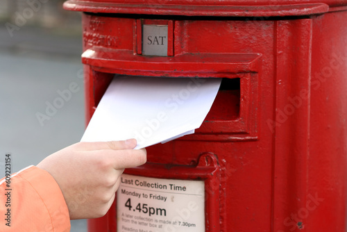 фотографія posting letter to red british postbox on street