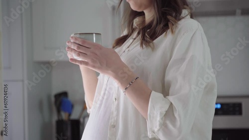 Pregnant woman drinking coffee. Caucasian girl enjoys her morning cup of coffee on her kitchen. Pregnancy and caffeine.