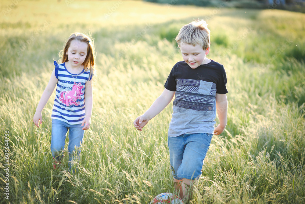 Boy and girl running through long grass playing soccer at the park. Aussie kids having fun outdoors in nature Boy and girl running through long grass playing soccer at the park. Aussie kids having fun outdoors in nature