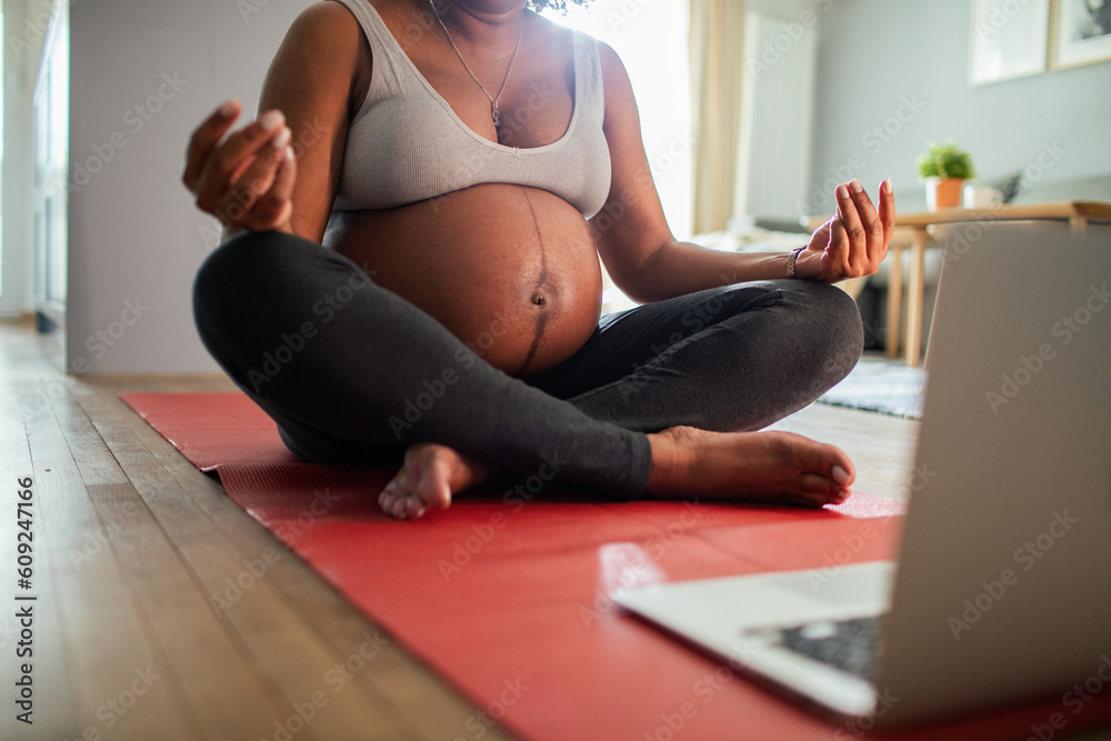 Young pregnant latina woman exercising at home wihle using a laptop