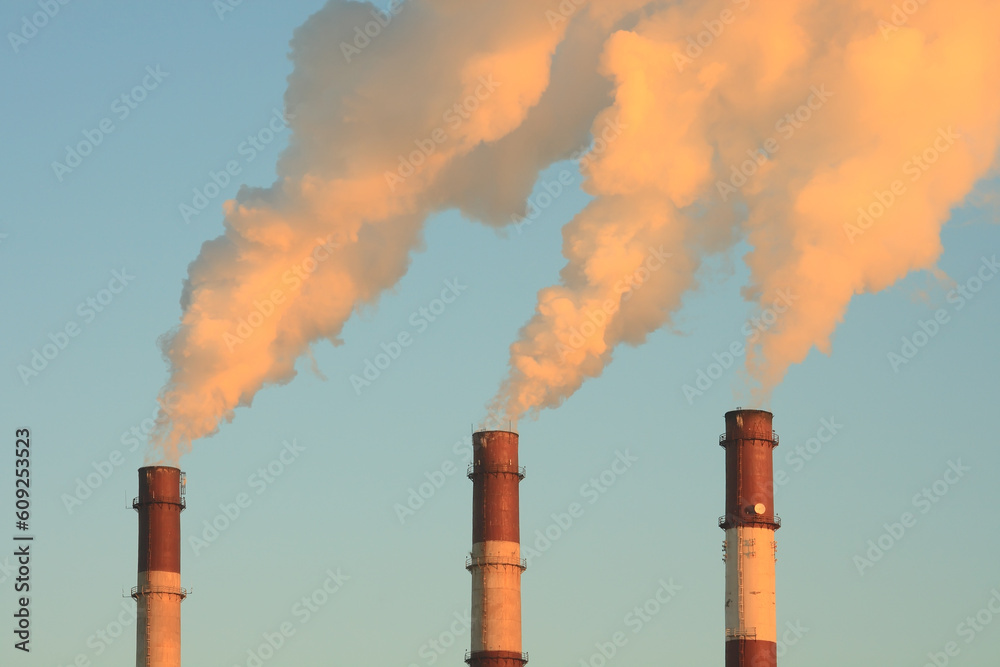 Three smoking chimneys lit by setting sun, against clear sky