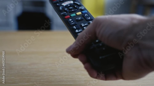 Hand picks up tv remote and proceeds to press buttons before removing it from the shot