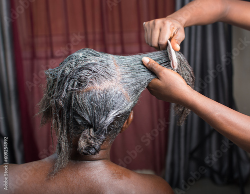 Hands of an African Nigerian stylist combing and applying relaxer cream to the  hair of a woman in saloon 