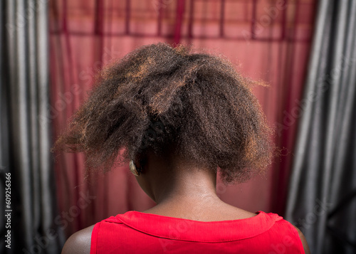 Rear view of a female african Nigerian lady back, showing her dark brownish and uncombed hair while sitting down