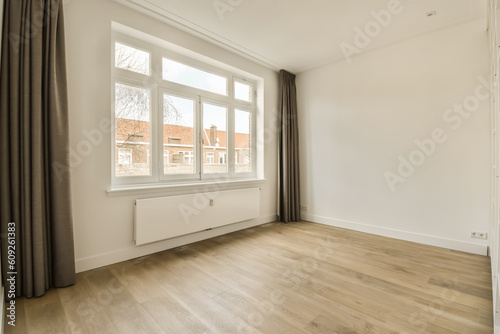 an empty room with wood flooring and large window overlooking the street in front of the house  on a sunny day