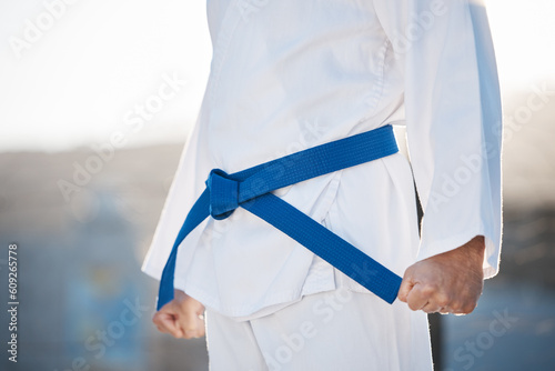 Karate, fitness and discipline with a sports man in gi, training in the city on a blurred background. Exercise, fighter or strong with a male athlete during a self defense workout for health closeup