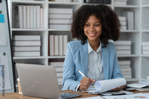 Project revenue and profit accounting African american businesswoman working with laptop financial charts and graphs checking and reading data details in financial paper documents at desk.