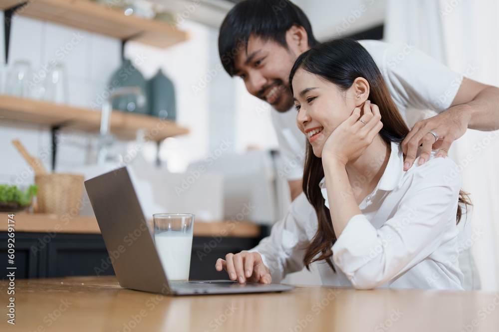 Young married couple showing happy smiling faces and using computers and notebooks to calculate household income and expenses while relaxing at home. Young married couple showing happy smiling faces and using computers and notebooks to calculate household income and expenses while relaxing at home.