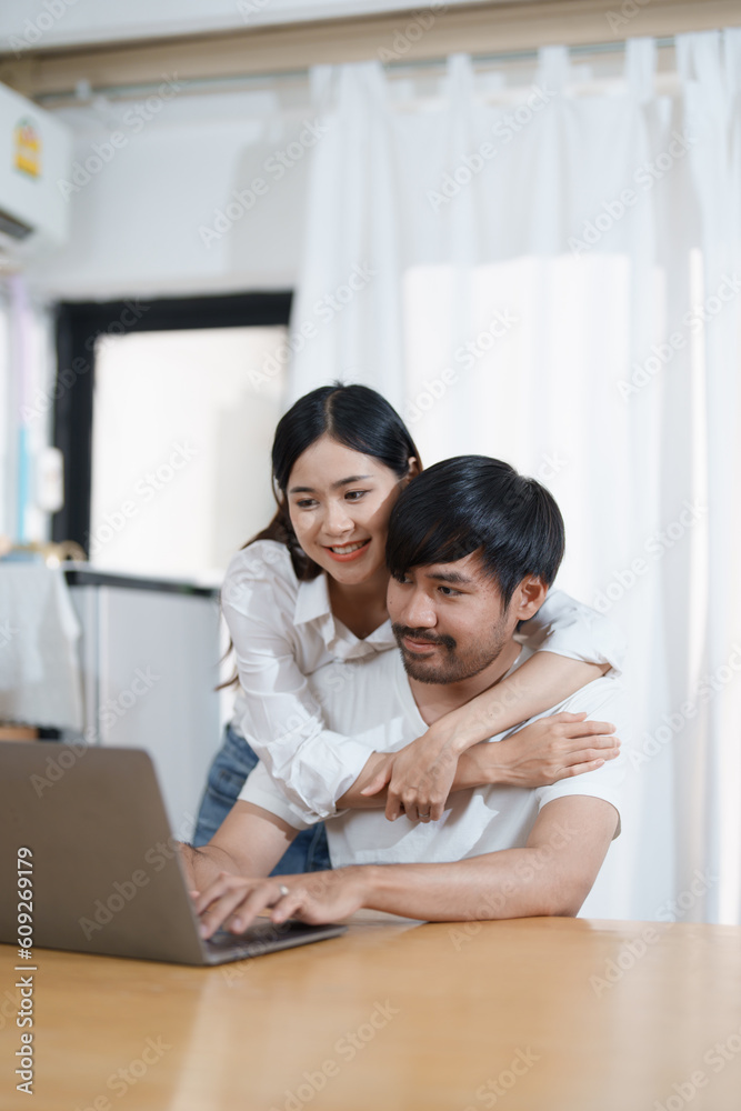 Young married couple showing happy smiling faces and using computers and notebooks to calculate household income and expenses while relaxing at home. Young married couple showing happy smiling faces and using computers and notebooks to calculate household income and expenses while relaxing at home.