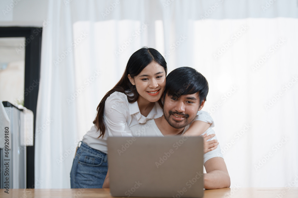 Young married couple showing happy smiling faces and using computers and notebooks to calculate household income and expenses while relaxing at home. Young married couple showing happy smiling faces and using computers and notebooks to calculate household income and expenses while relaxing at home.