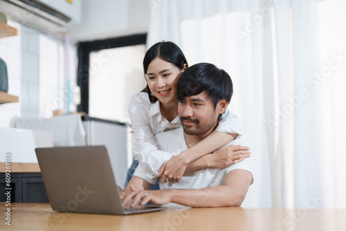 Young married couple showing happy smiling faces and using computers and notebooks to calculate household income and expenses while relaxing at home.