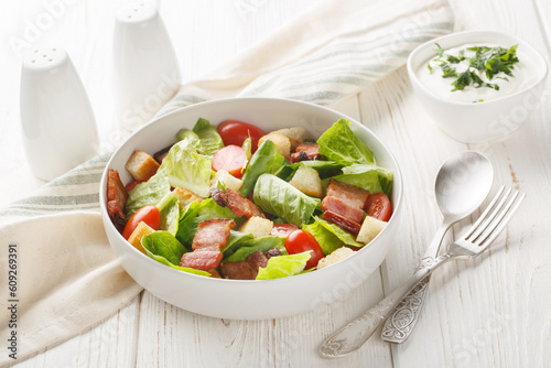 BLT salad with romaine lettuce, pieces of crispy bacon, tomatoes, crunchy croutons, and a creamy garlic dressing closeup on the plate on the table. Horizontal