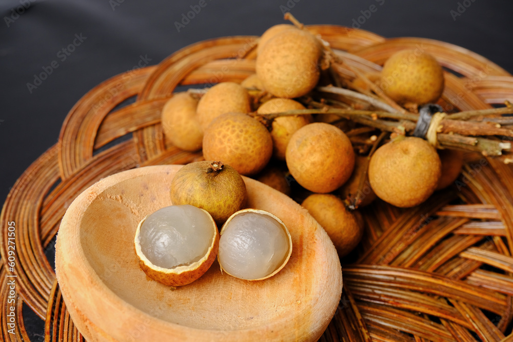 peeled and unpeeled longan fruits in a wooden bowl