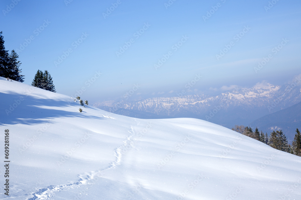Fototapeta premium Snow-covered hill with footprints leading into the distance.