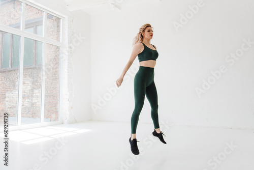 Active strong woman with blond hair jumping at white hall