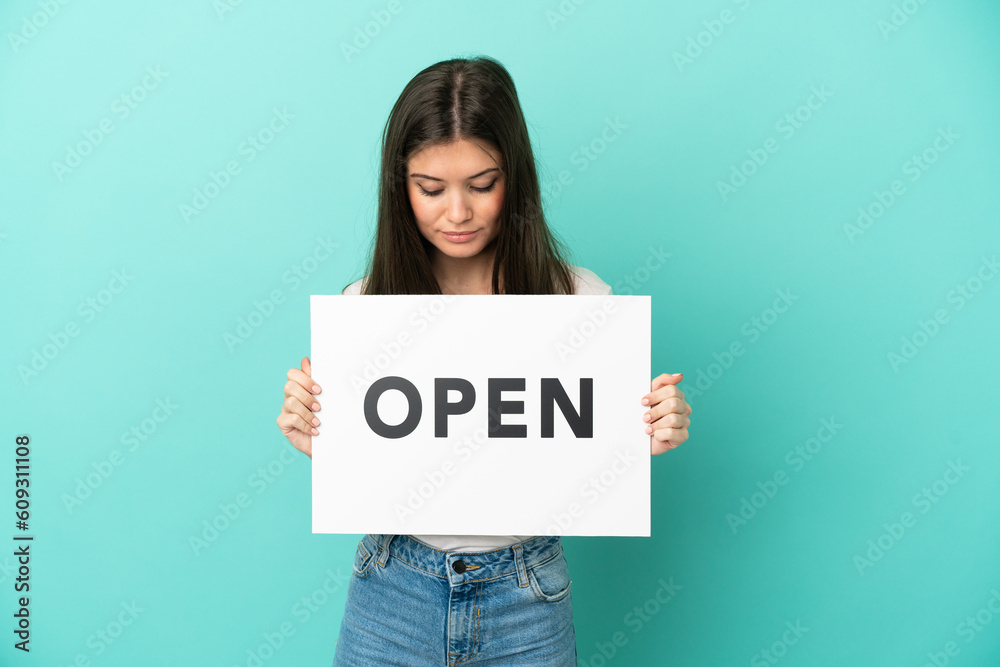Young caucasian woman isolated on blue background holding a placard with text OPEN Young caucasian woman isolated on blue background holding a placard with text OPEN