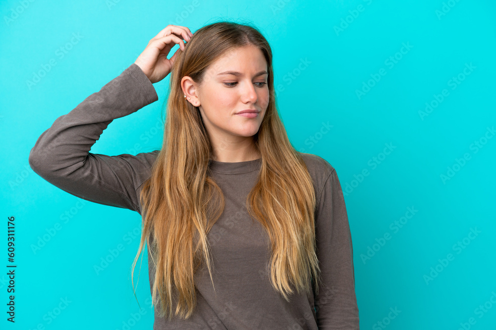Fototapeta premium Young blonde woman isolated on blue background having doubts while scratching head