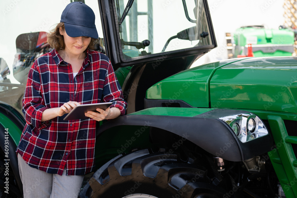 Woman farmer with a digital tablet on the background of an agricultural tractor	