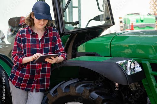 Woman farmer with a digital tablet on the background of an agricultural tractor 