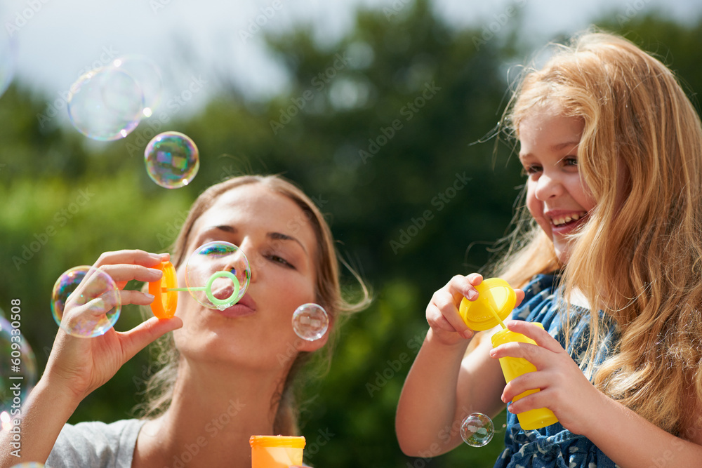 Mother blowing bubbles with daughter, happiness outdoor with bonding and love with childhood and parenting. Woman playing outside with young girl, mom and female child with fun activity together