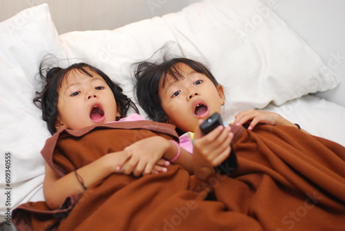 two beautiful Asian girls watching TV in the room while scared