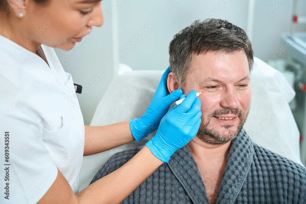 Health worker at consultation examines the face of middle-aged patient Health worker at consultation examines the face of middle-aged patient