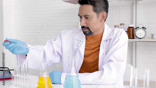 Professional scientist with beard drop liquid blue and yellow solution, teacher analyzed experimental results in science room, medical science test tube with chemical fluid testin in laboratory lab. photo