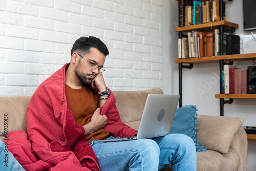 Young sick ill mentally depressed anxious man sitting home alone wrapped in blanket watching sad movies on laptop computer. Despair young male stressed after relationship break out heartbroken