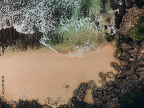 Aerial top view of aptivating beach with rocky foreground, crashing waves, and a reflective body of water. Moody atmosphere, close-ups of rocks. photo