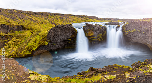 beautiful waterfall falling in the middle of mountains in iceland with a clear day and a ray of sun © Marco