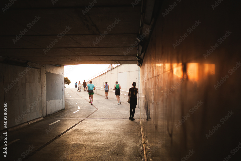 silhouettes of people walking and doing sports activities through a tunnel, tunnel with sunlight flares in the exit