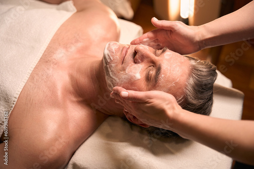 Qualified beautician cleansing man face before beauty procedure