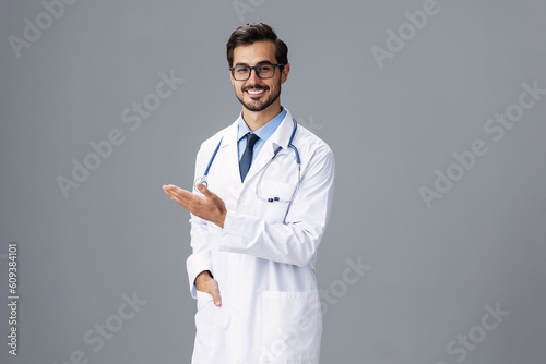 Male smile doctor in a white coat and glasses for vision and a stethoscope looks at the camera with his hands open on a gray isolated background, copy space, space for text, health