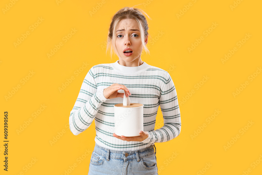 Allergic young woman with tissue box on yellow background Allergic young woman with tissue box on yellow background