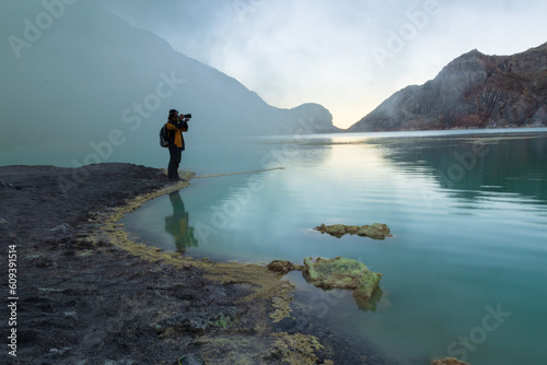 Woman traveler taking pictures at turquoise lake with smoke sulfur in the morning. The world's largest acidic lake,inside the crater of Kawah Ijen volcano in East Java, Indonesia.