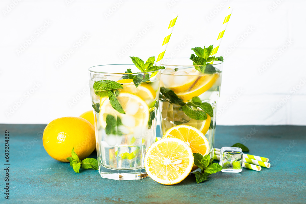 Fototapeta premium Lemonade in glass on white table with fresh lemons and mint. Cold summer drink.