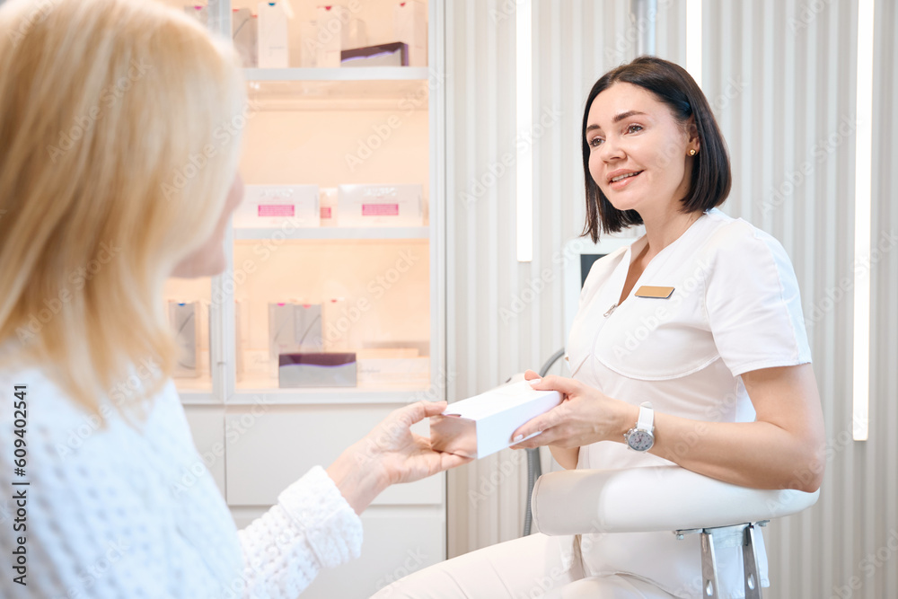 Cosmetologist gives his client box with cosmetic product Cosmetologist gives his client box with cosmetic product