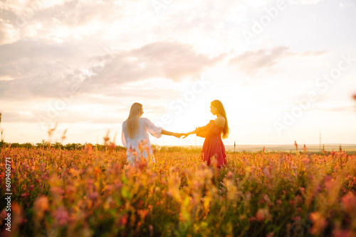 Portrait of a two beautiful woman posing in a field with flowers. Nature, vacation, relax and lifestyle. Summer landscape.
