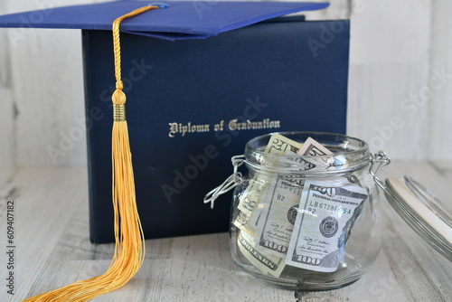 Graduation cap mortarboard tassel on diploma by a jar of money cash, concept school loans debt education costs photo