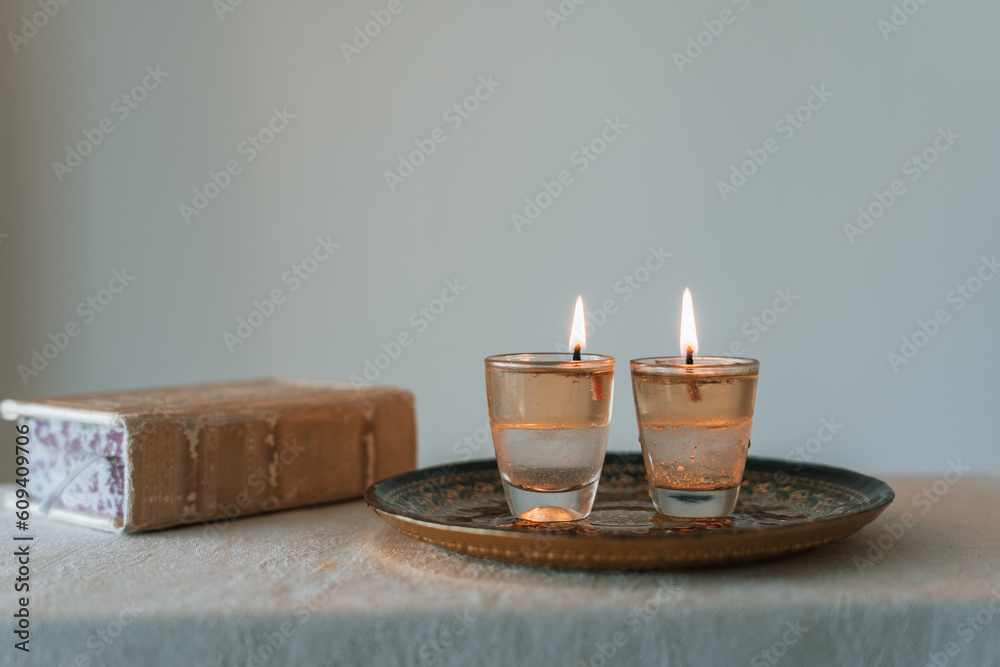 On the table are two candles lit on shabbat and a siddur (religious jewish prayer book). Jewish