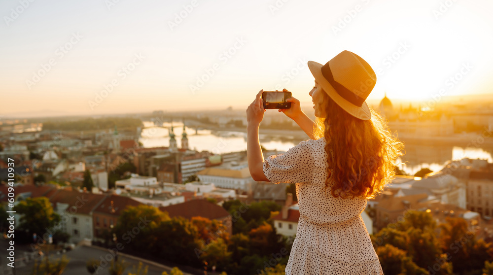 Tourist woman shoots a city landscape at dawn on a smartphone. Travel in Europe. Blogging, travel, tourism, technology concept.