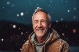 Portrait of smiling senior man standing outdoors with snowflakes falling on him