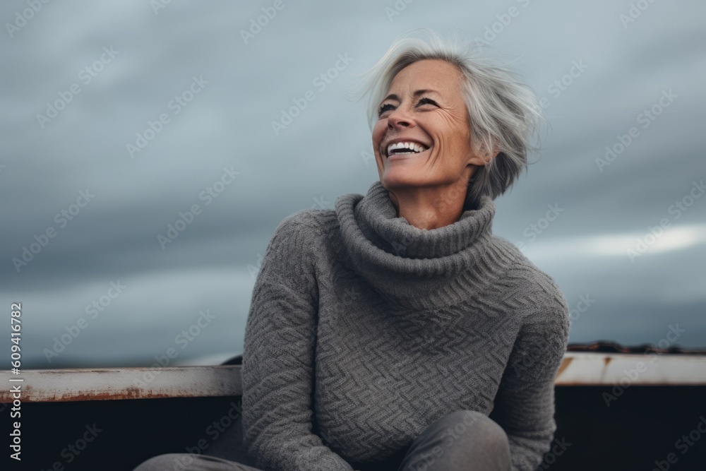 Fototapeta premium Portrait of happy senior woman in grey sweater against cloudy sky.